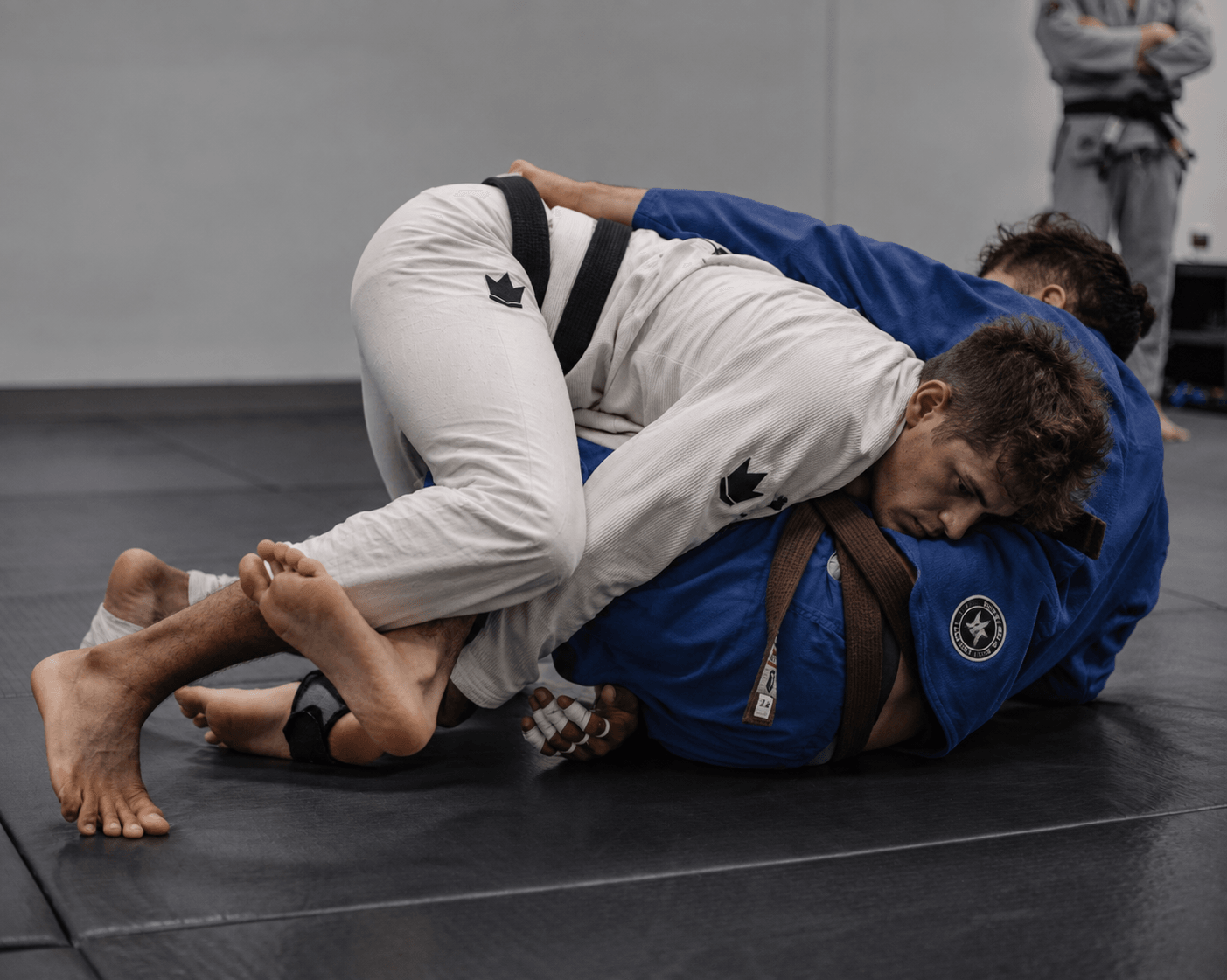 Two students rolling on the mats — white gi passing the guard of a blue gi
