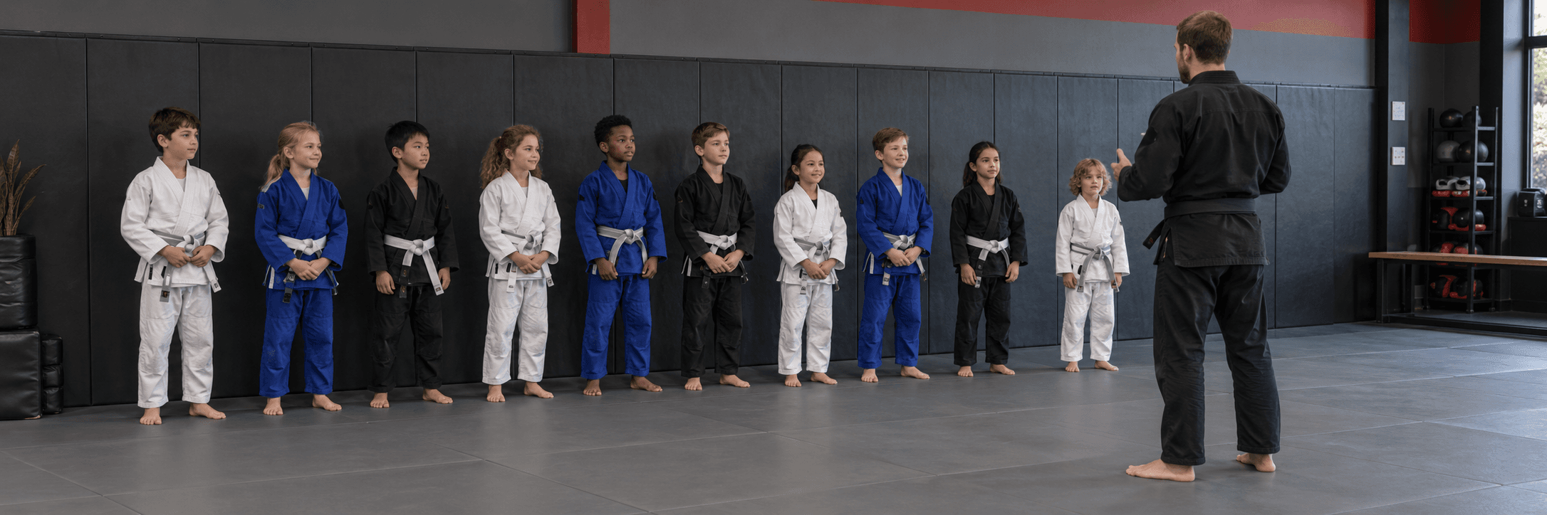 Kids in gis lined up on the mats facing a coach
